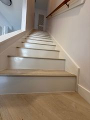 Staircase with light-colored carpeted treads, white risers, and a wooden handrail on the right wall.