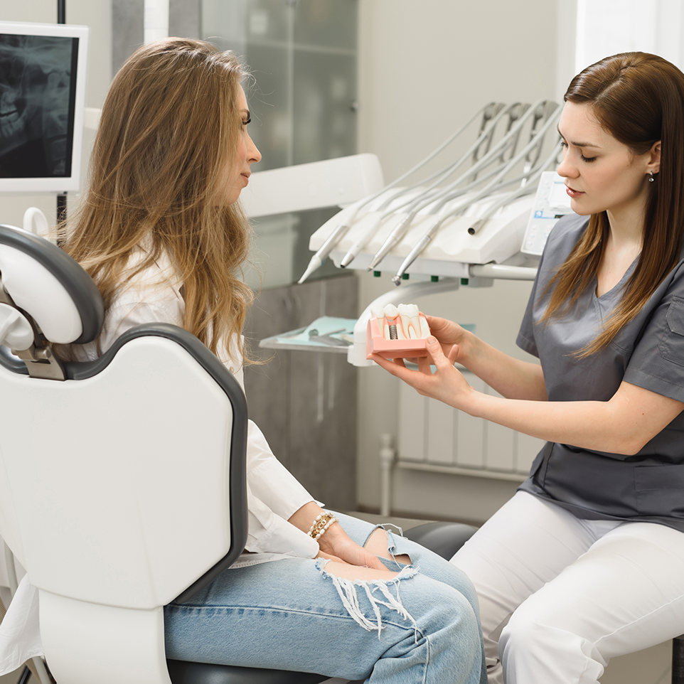 A woman is sitting in a dental chair talking to a dentist who is holding a model of teeth.