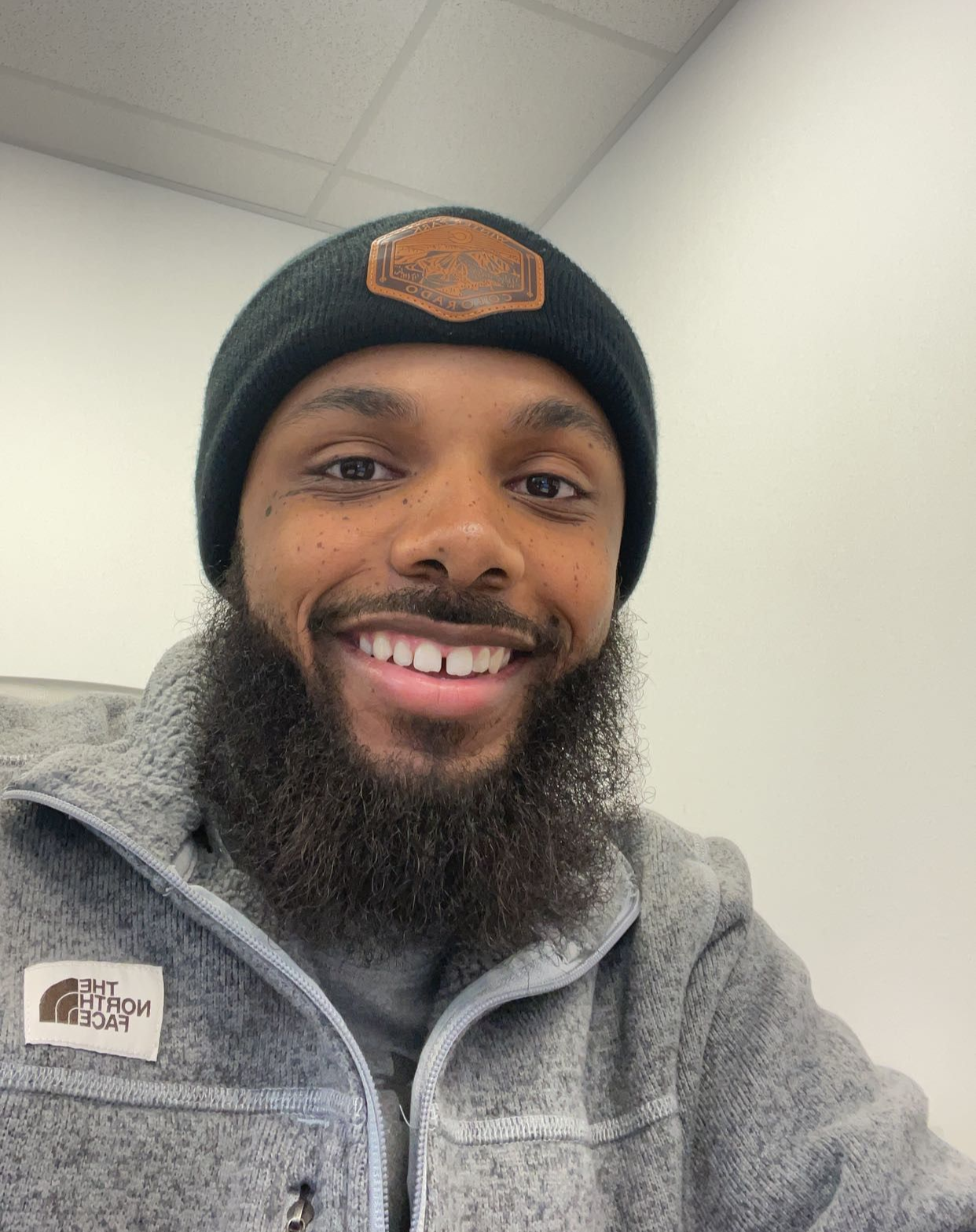 Smiling man in a black beanie and gray fleece jacket indoors under bright lights