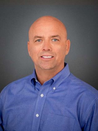 Smiling bald man in a blue button-down shirt against a gray background