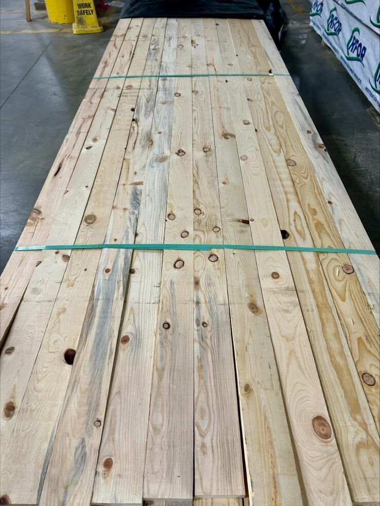Stacked wooden planks secured with green straps in a warehouse aisle.