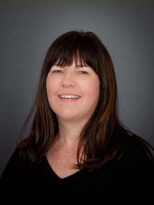 Head-and-shoulders portrait of a smiling person with long dark hair against a gray background