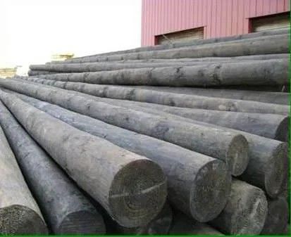 Stacked large dark concrete pipes beside a red building