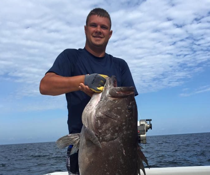 Man holding a large fish on a boat with open ocean and cloudy sky in the background