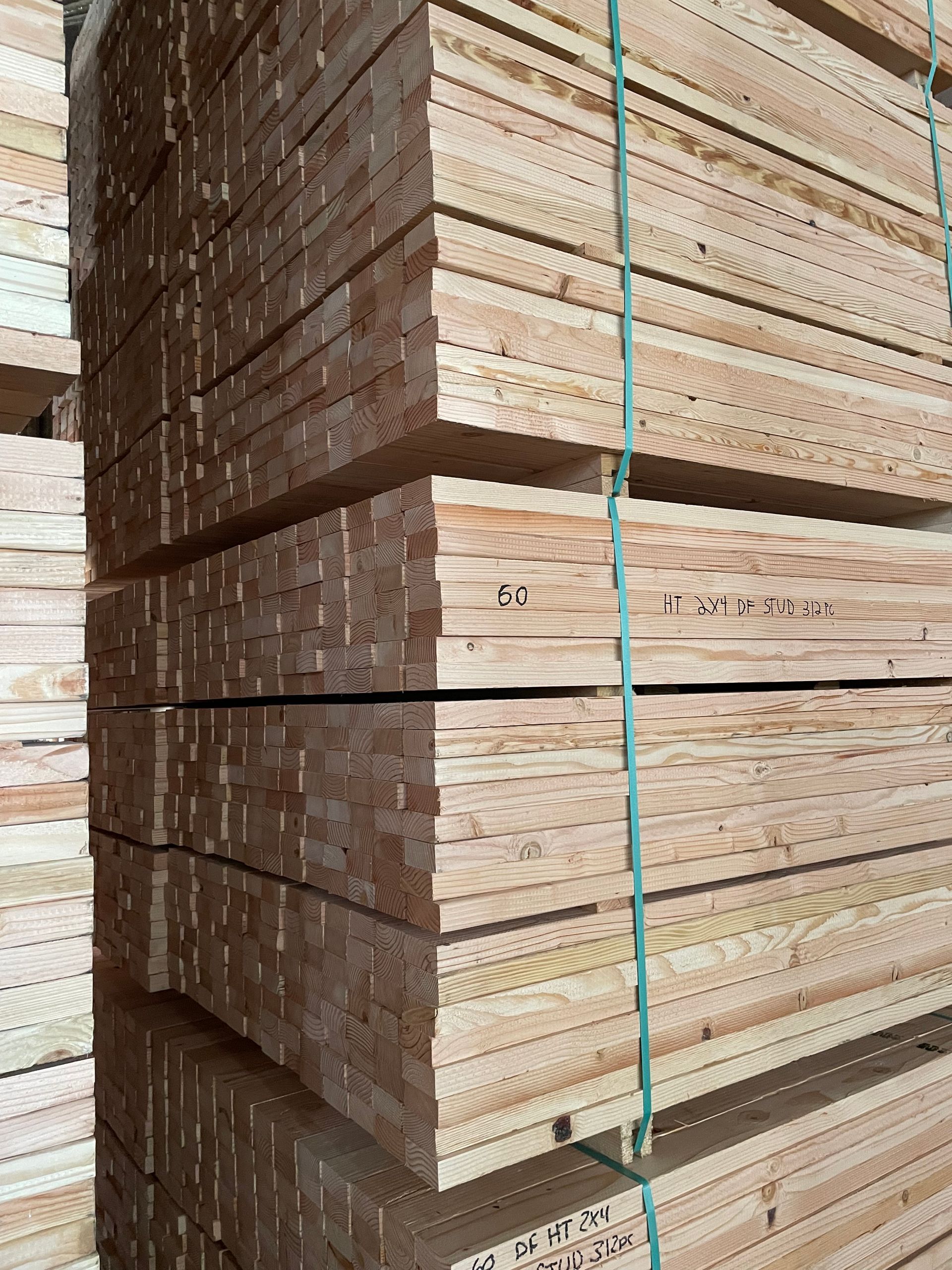 Stacks of bundled wooden planks strapped with green bands in a lumberyard