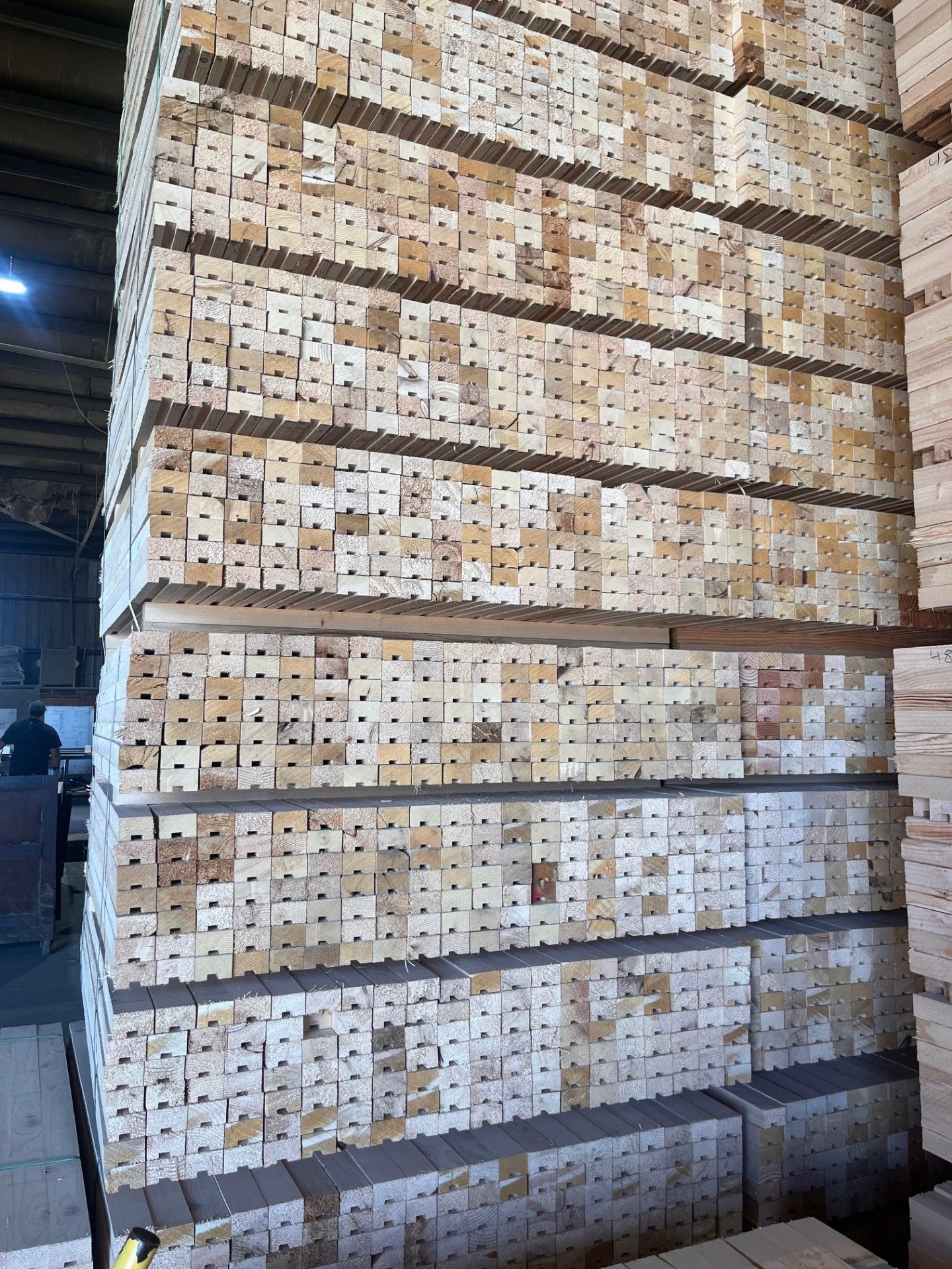 Stacked wooden crates in a warehouse, arranged in tall rows beside a metal beam.