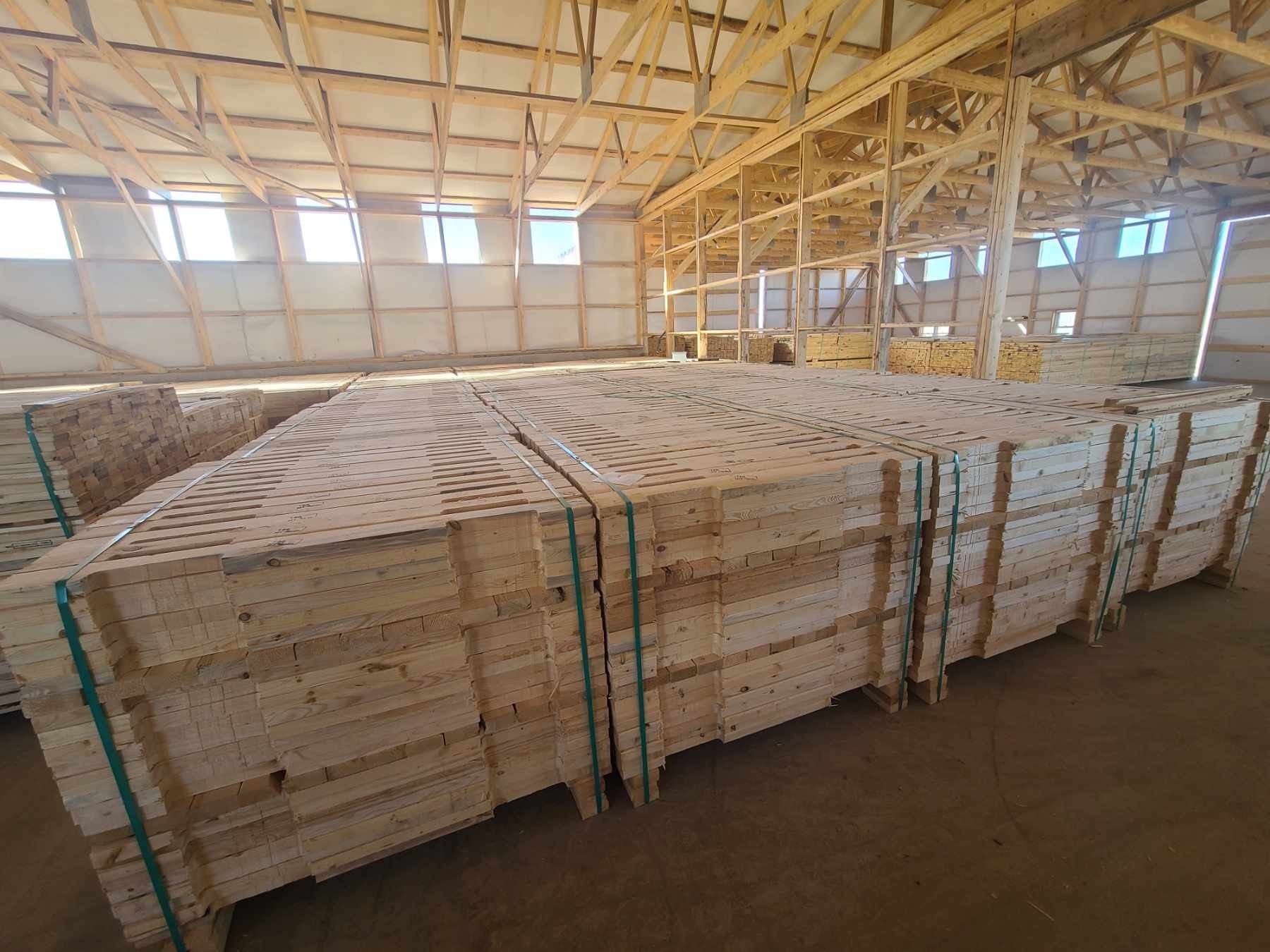 Stacked white lumber bundles strapped in a warehouse with yellow metal shelving.