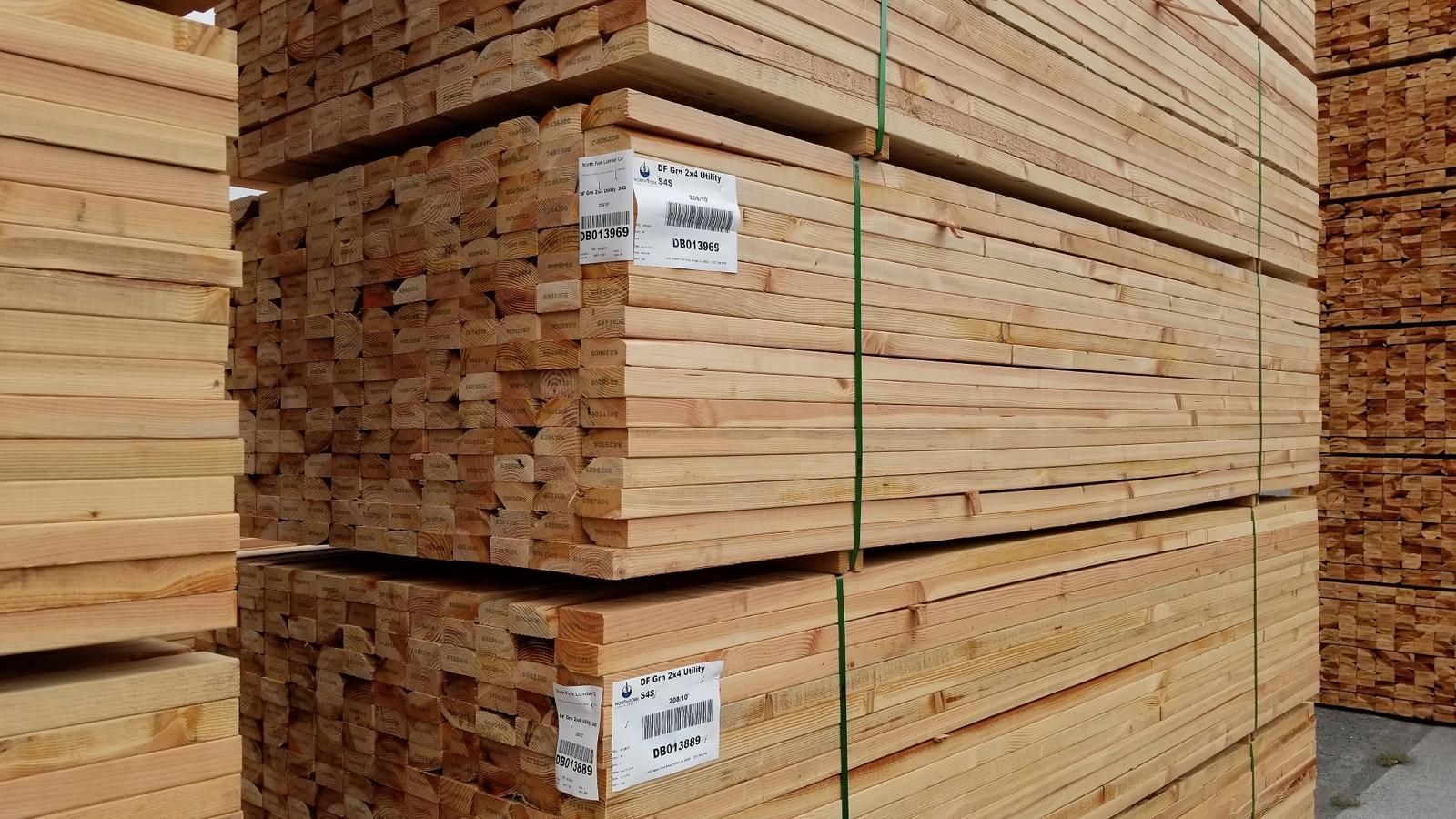 Stacks of bundled lumber in a warehouse, secured with green straps and labeled tags.