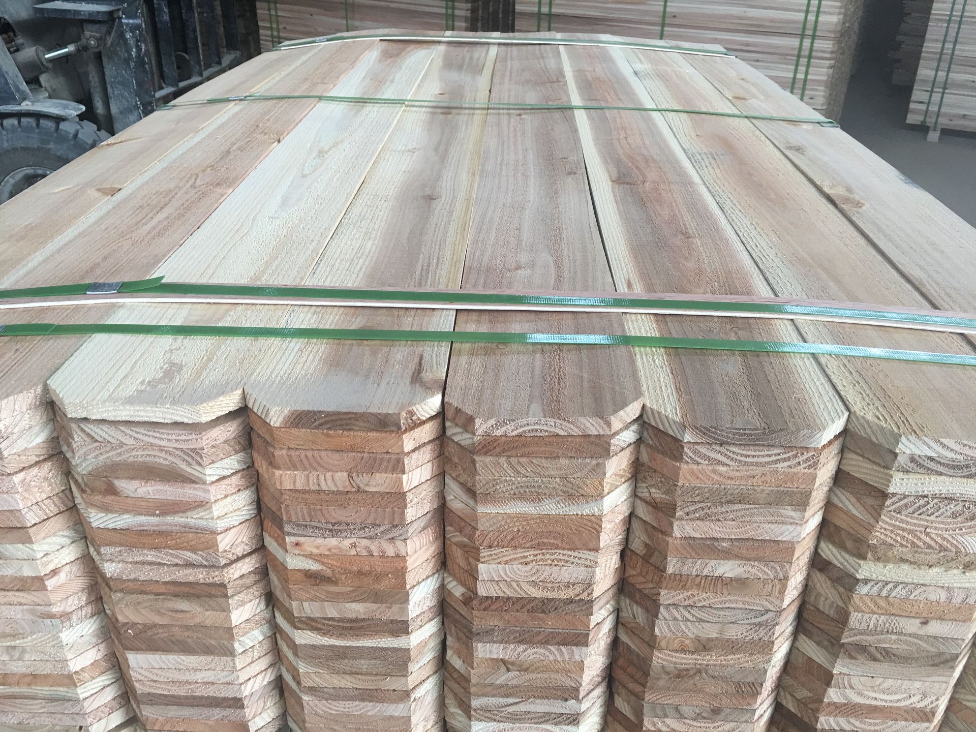 Stacked rough wooden planks bound with green straps in a lumber yard