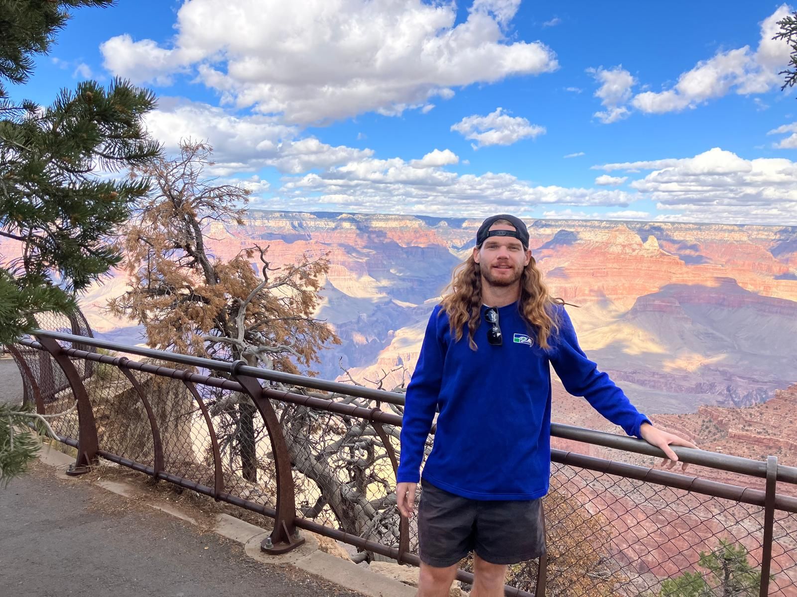 Person in blue jacket standing by a railing at the Grand Canyon under a partly cloudy sky