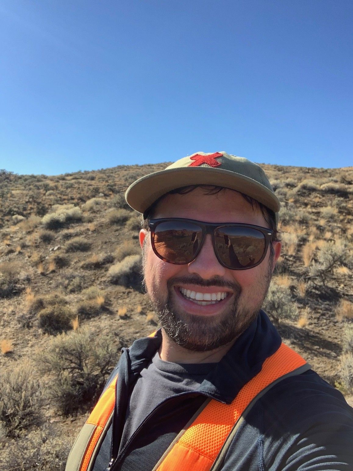 Smiling hiker in sunglasses and cap on a dry desert trail under a clear blue sky