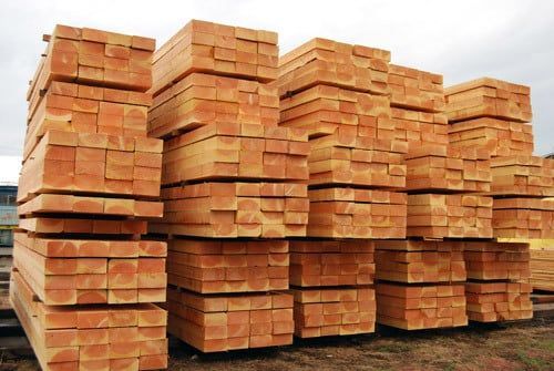 Stacks of lumber planks piled outdoors on a grassy site under a cloudy sky