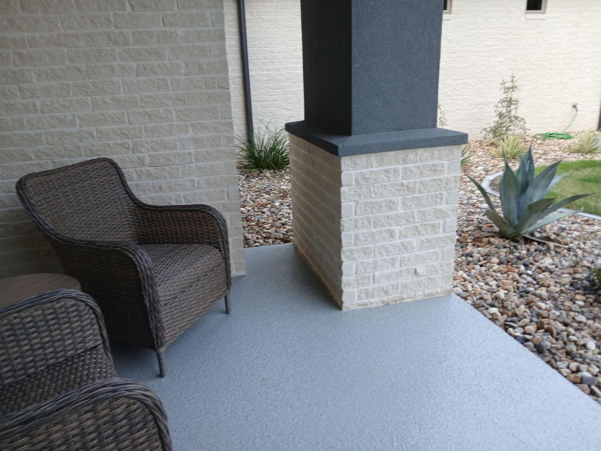 Wicker chairs on a gray porch near a brick pillar and landscaping.