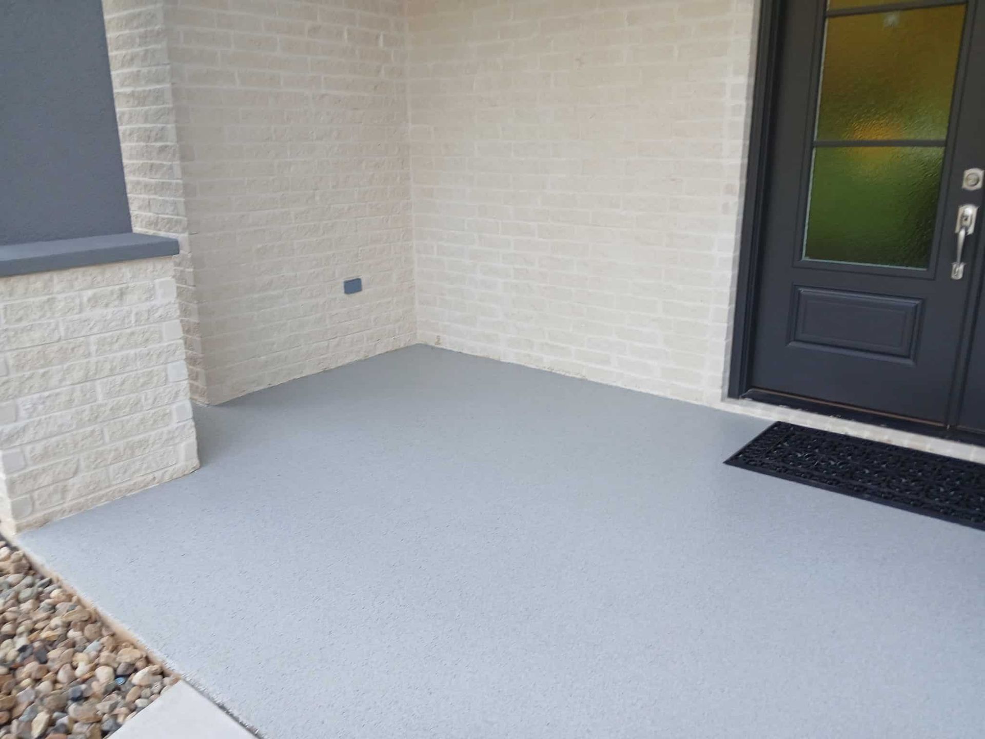 Gray painted porch with gray door, brick walls, and a black doormat.