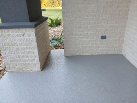 Gray concrete porch with textured light brick walls and a column. Green hose visible.