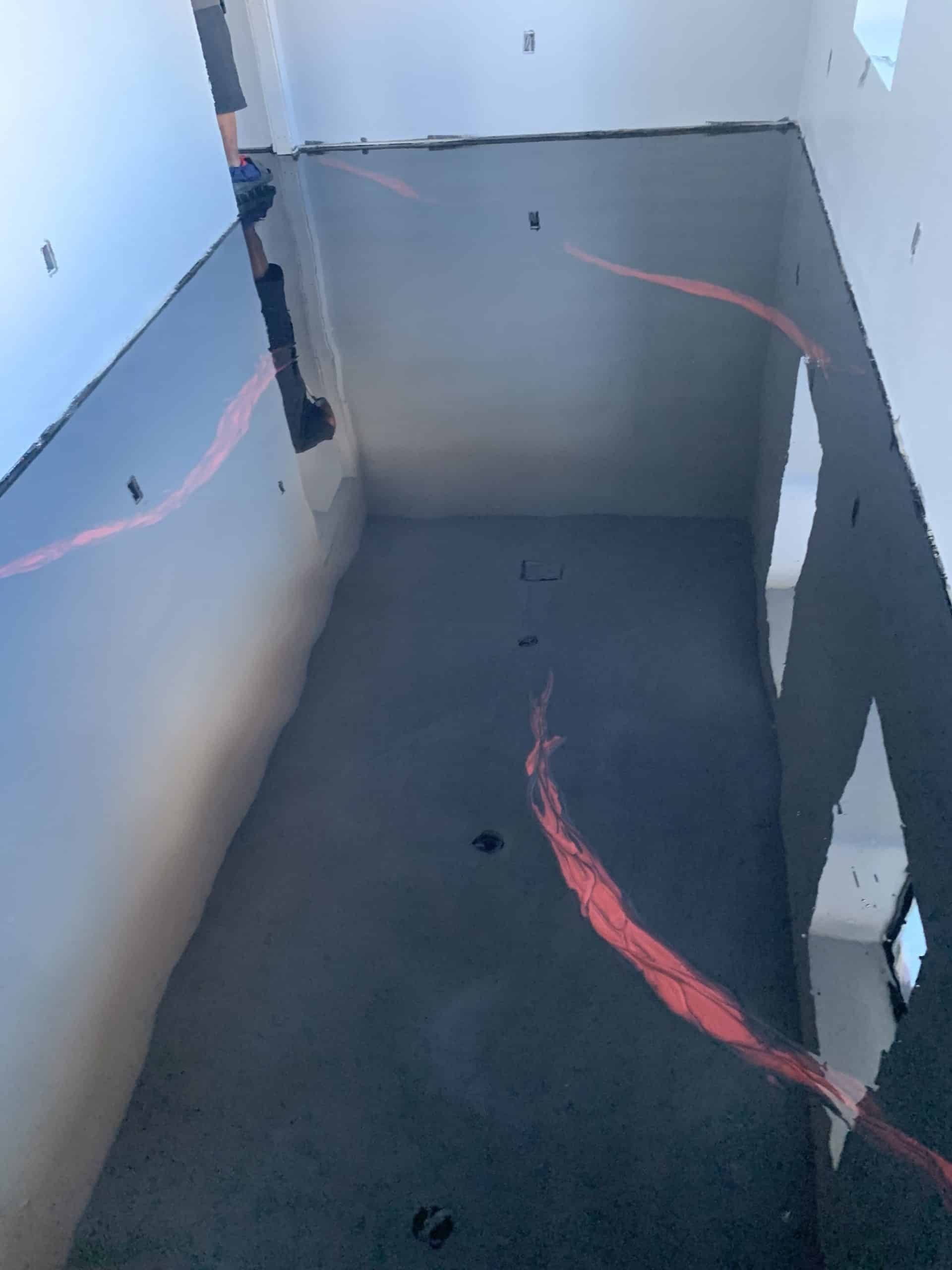 Empty room with dark gray floor, gray walls, and red streaks. Light from upper left.