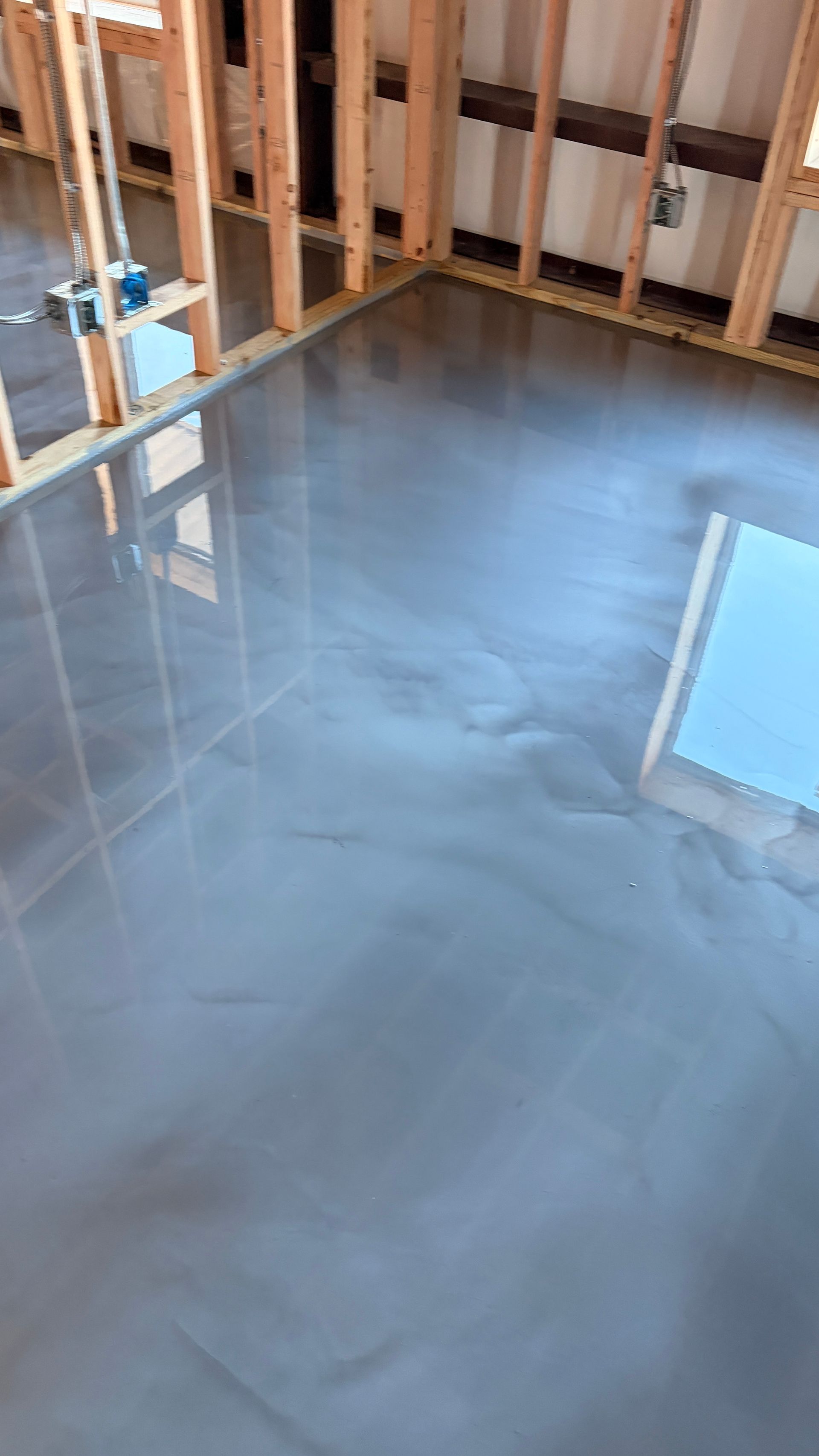 Interior of a room with gray epoxy flooring and exposed wooden framing.