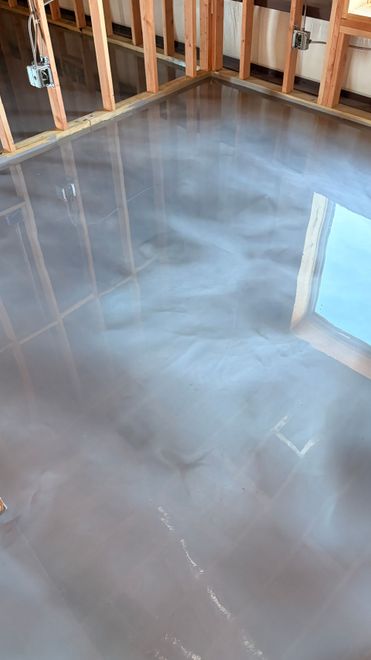 Shiny, gray epoxy floor in a room under construction with exposed wooden framing.
