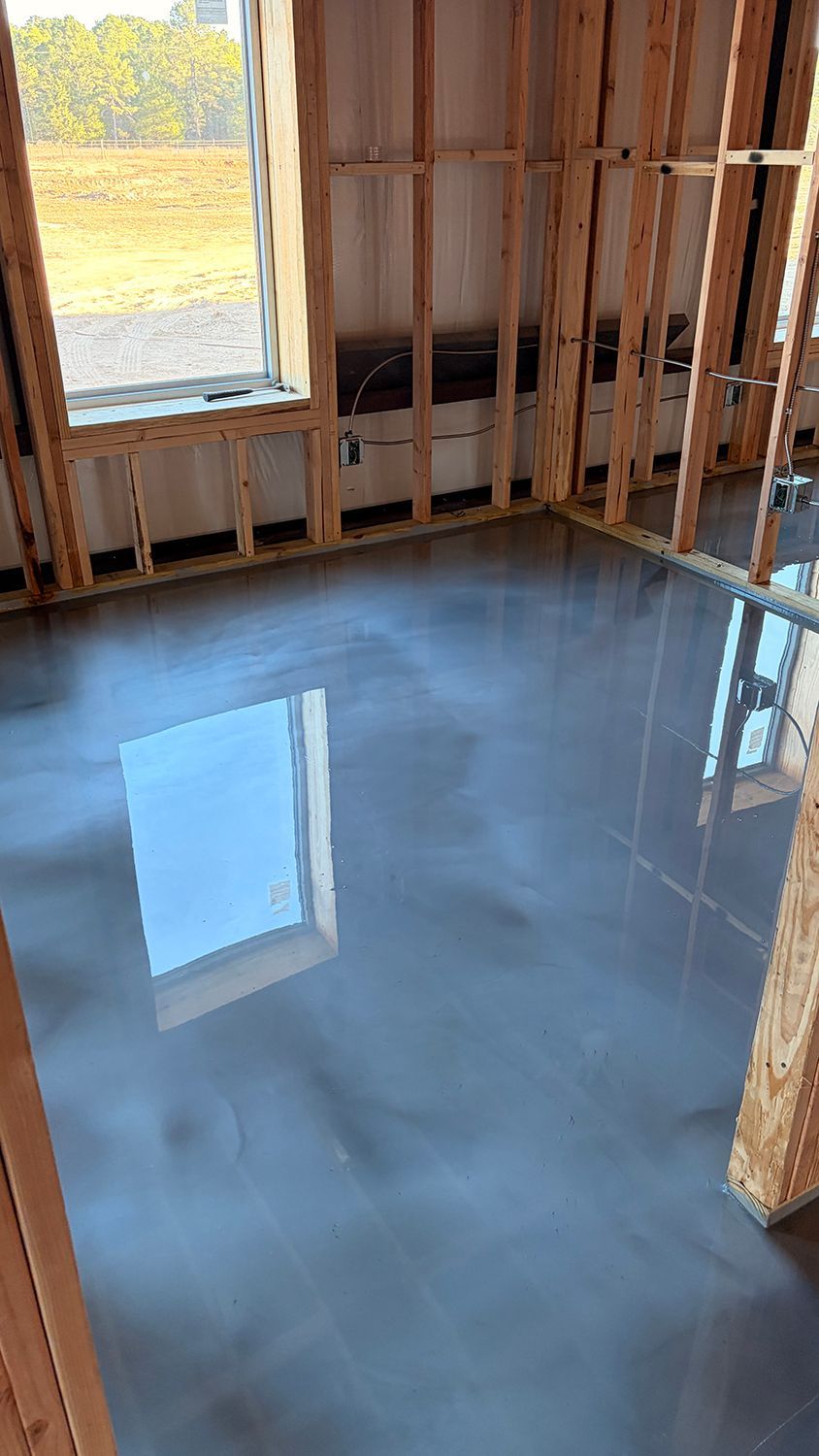 Room under construction with a reflective gray floor and wooden framing. Sunlight reflects off the floor.