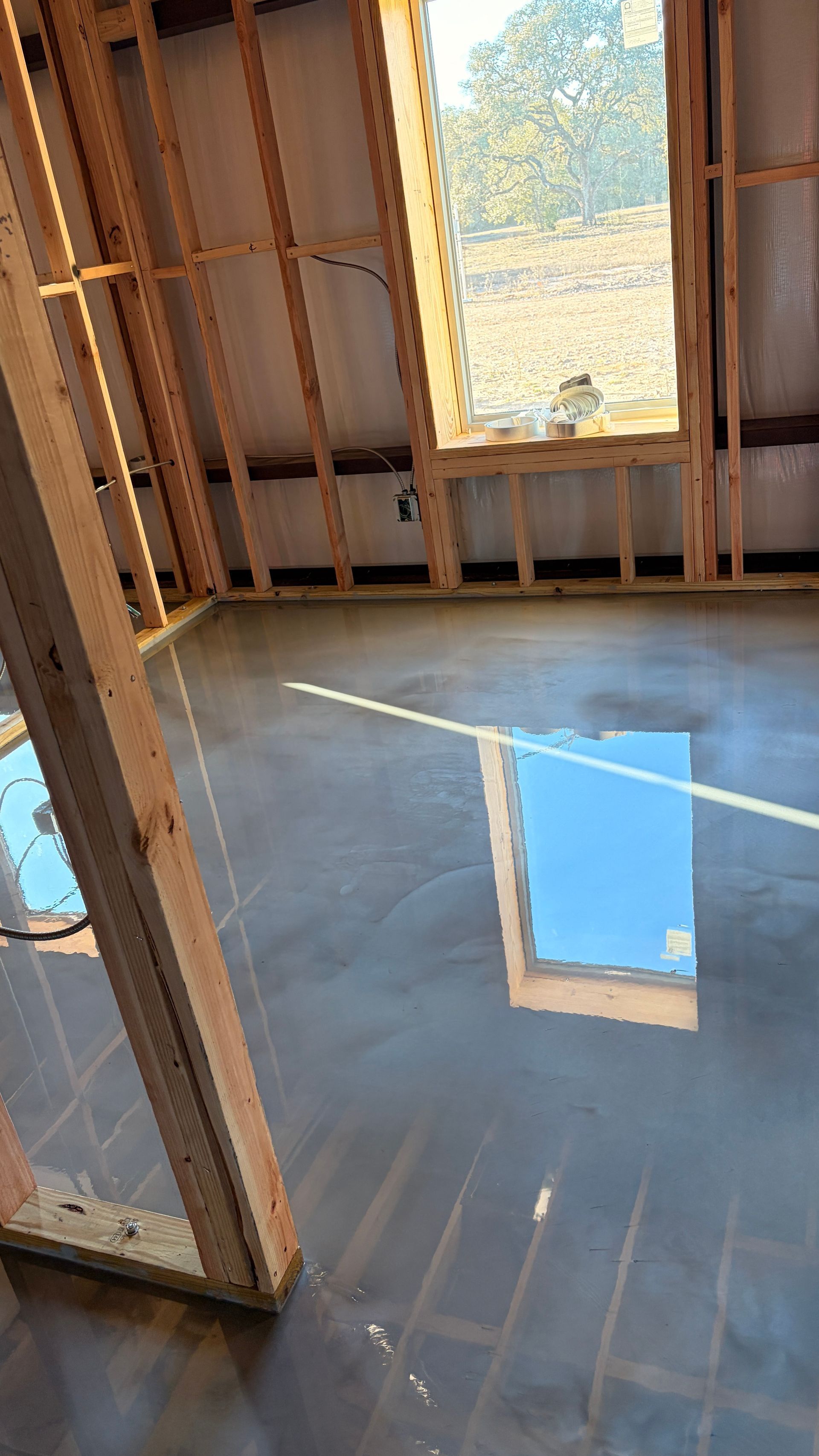 Interior of a building under construction. Unfinished wooden frame, concrete floor, window with sky view.