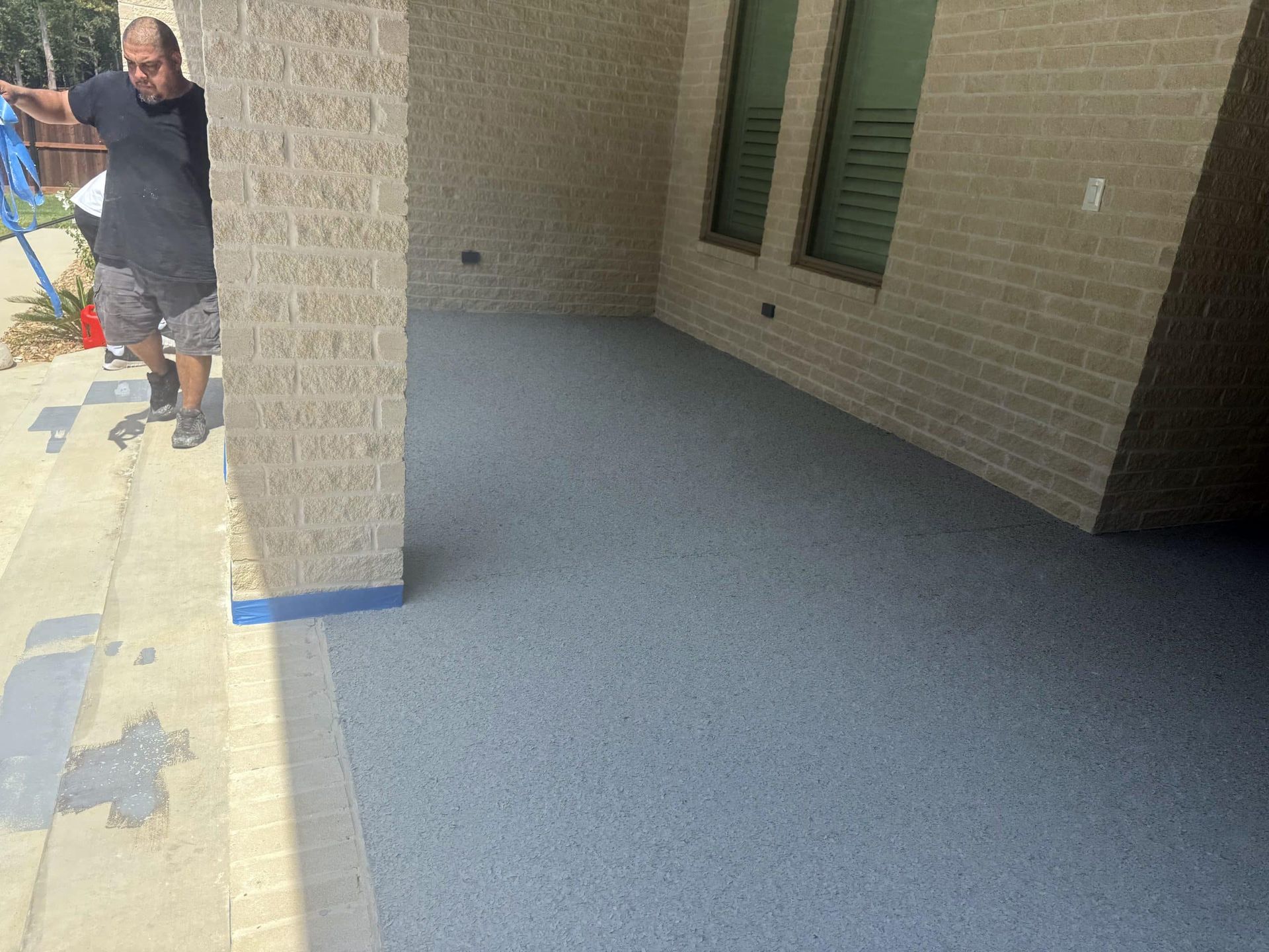 A man stands near a blue speckled concrete patio next to a brick wall.