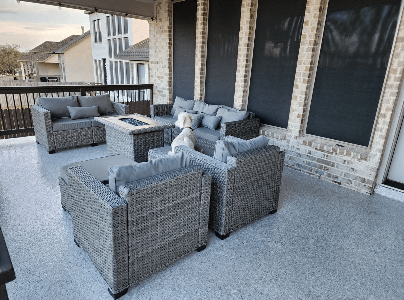 Outdoor patio with gray wicker furniture, fire pit, and a small dog.