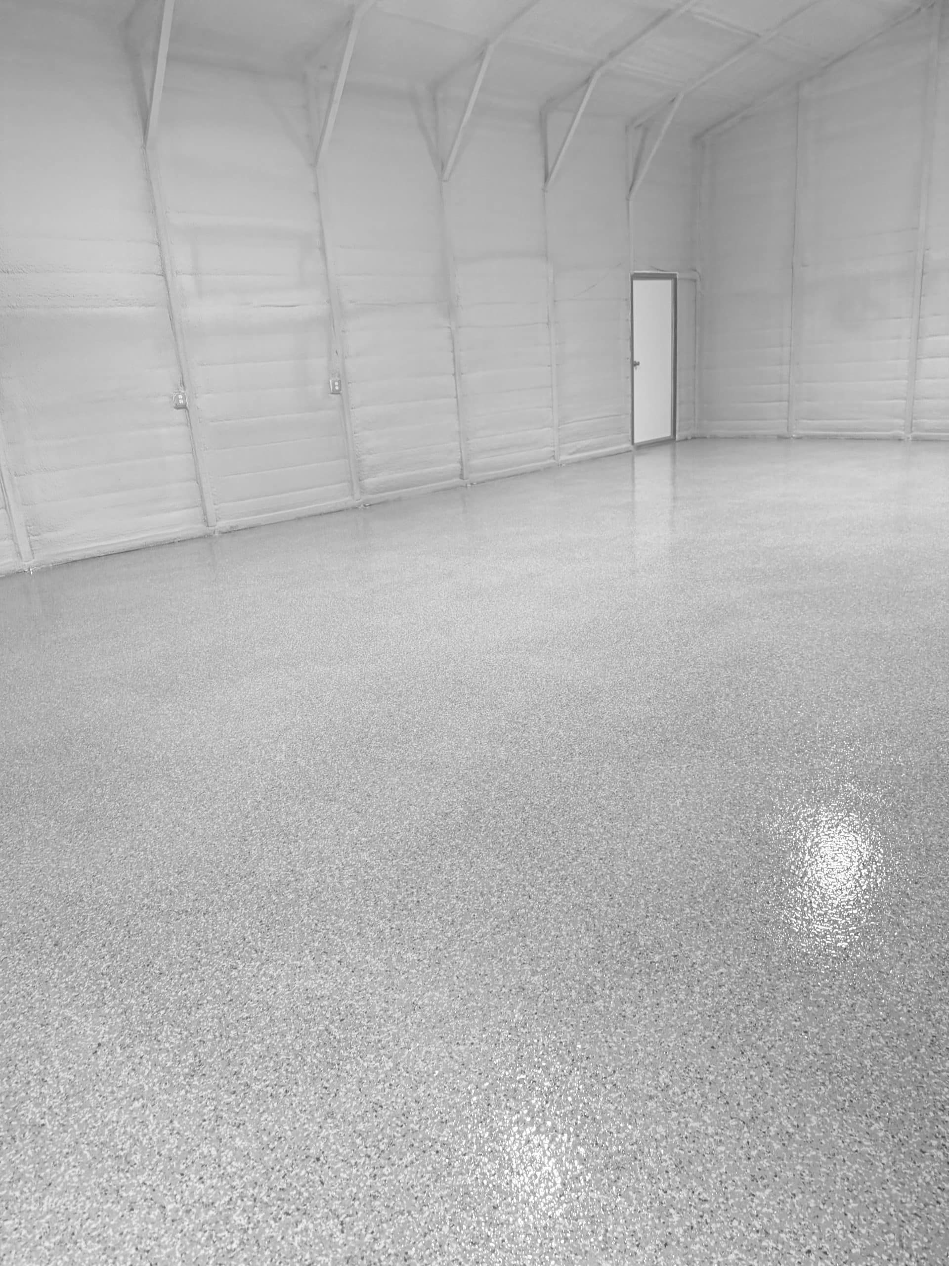 Spacious, empty warehouse interior with a speckled, reflective floor and a door at the back.