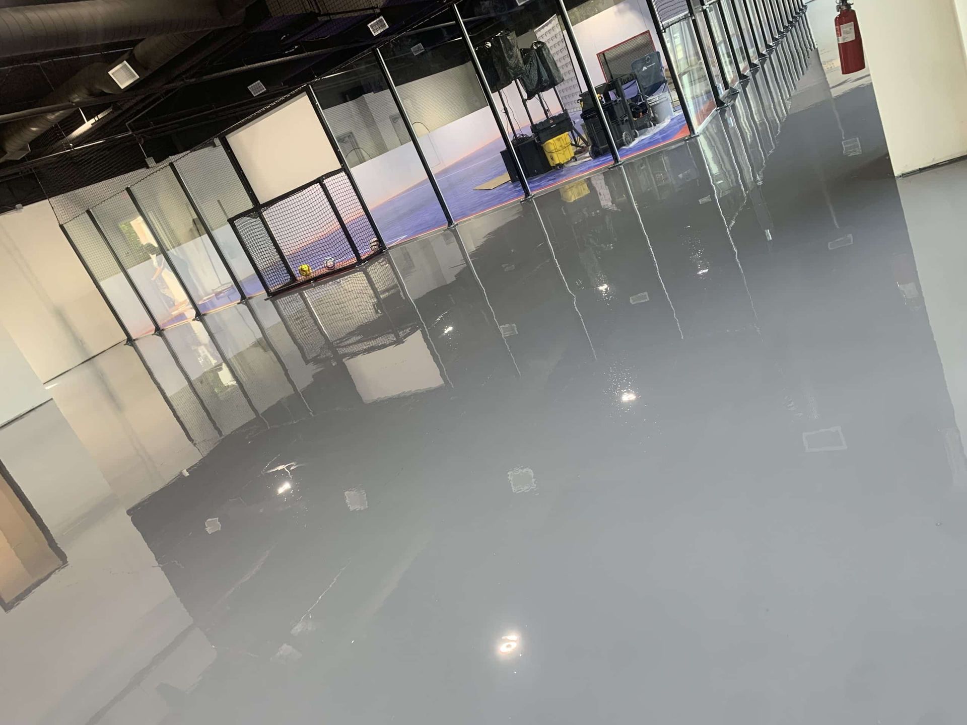 Gray, glossy epoxy floor reflecting a modern interior with glass walls and bright lights.