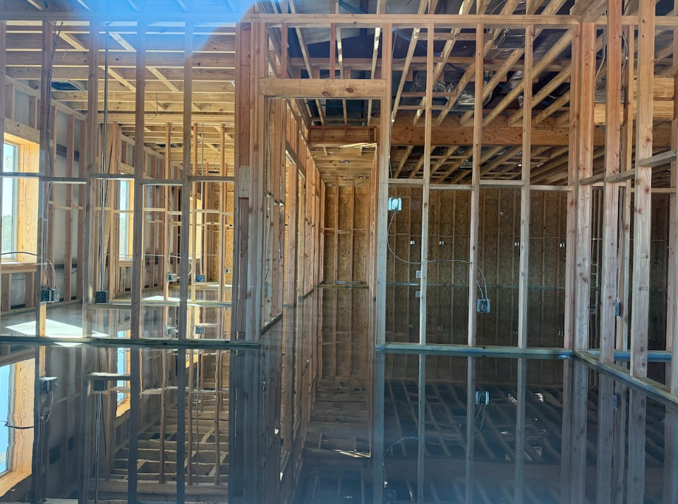 Interior view of a building under construction, showing wooden framing and a flooded floor reflecting the structure.
