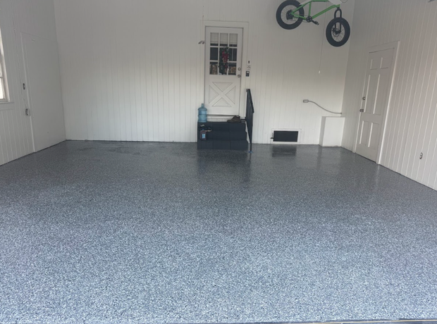 Empty garage with a gray speckled epoxy floor, white walls, and a green bicycle hanging.