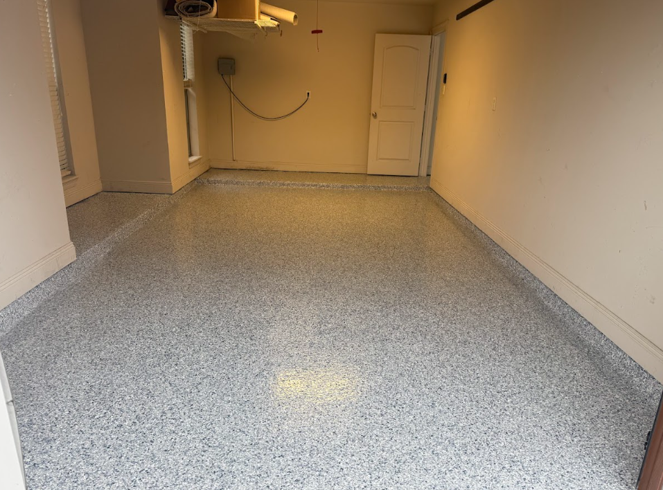 Garage with gray speckled epoxy flooring, white door, tan walls.