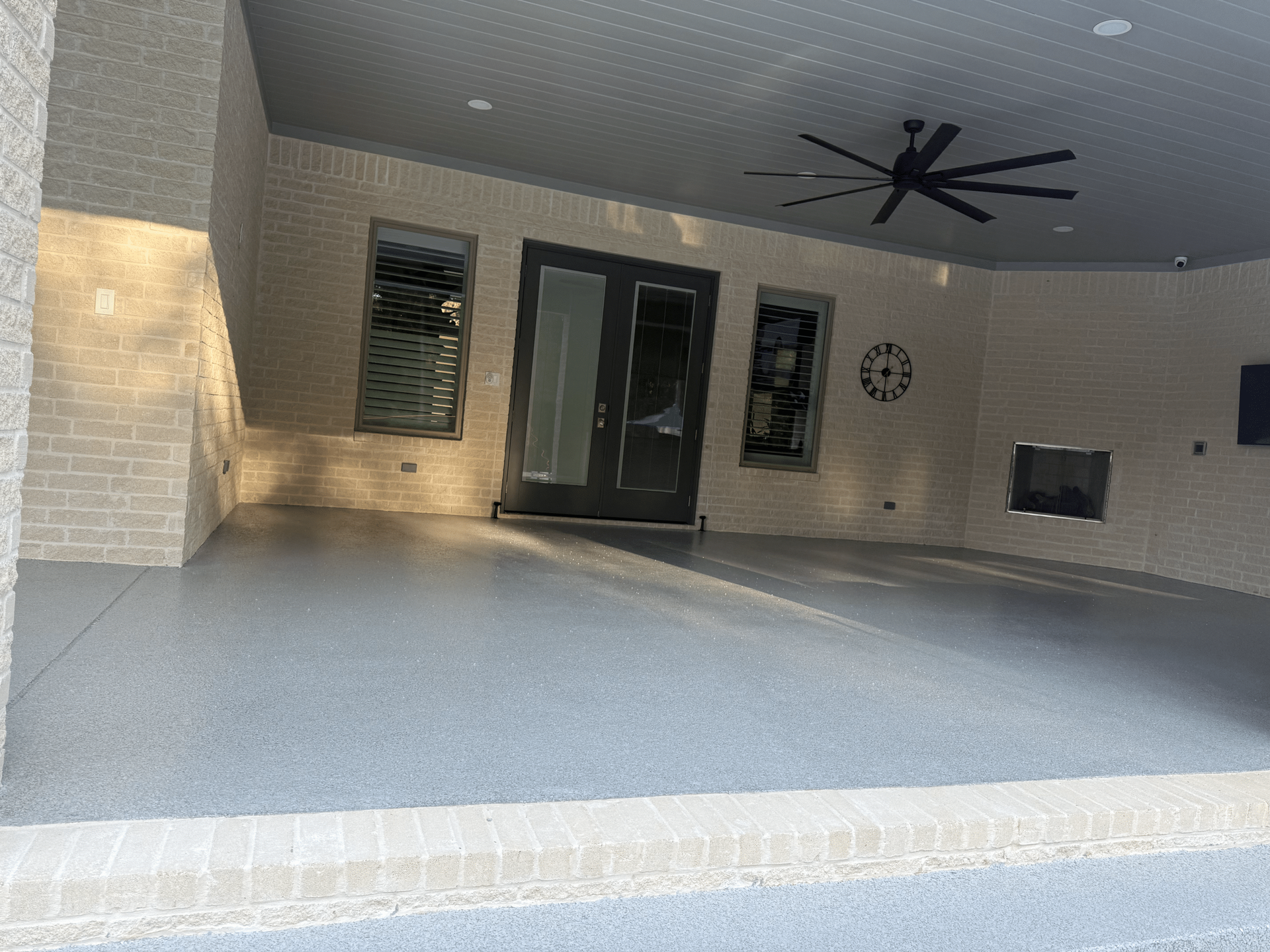 Covered outdoor patio with a gray floor, brick walls, a ceiling fan, and a fireplace.