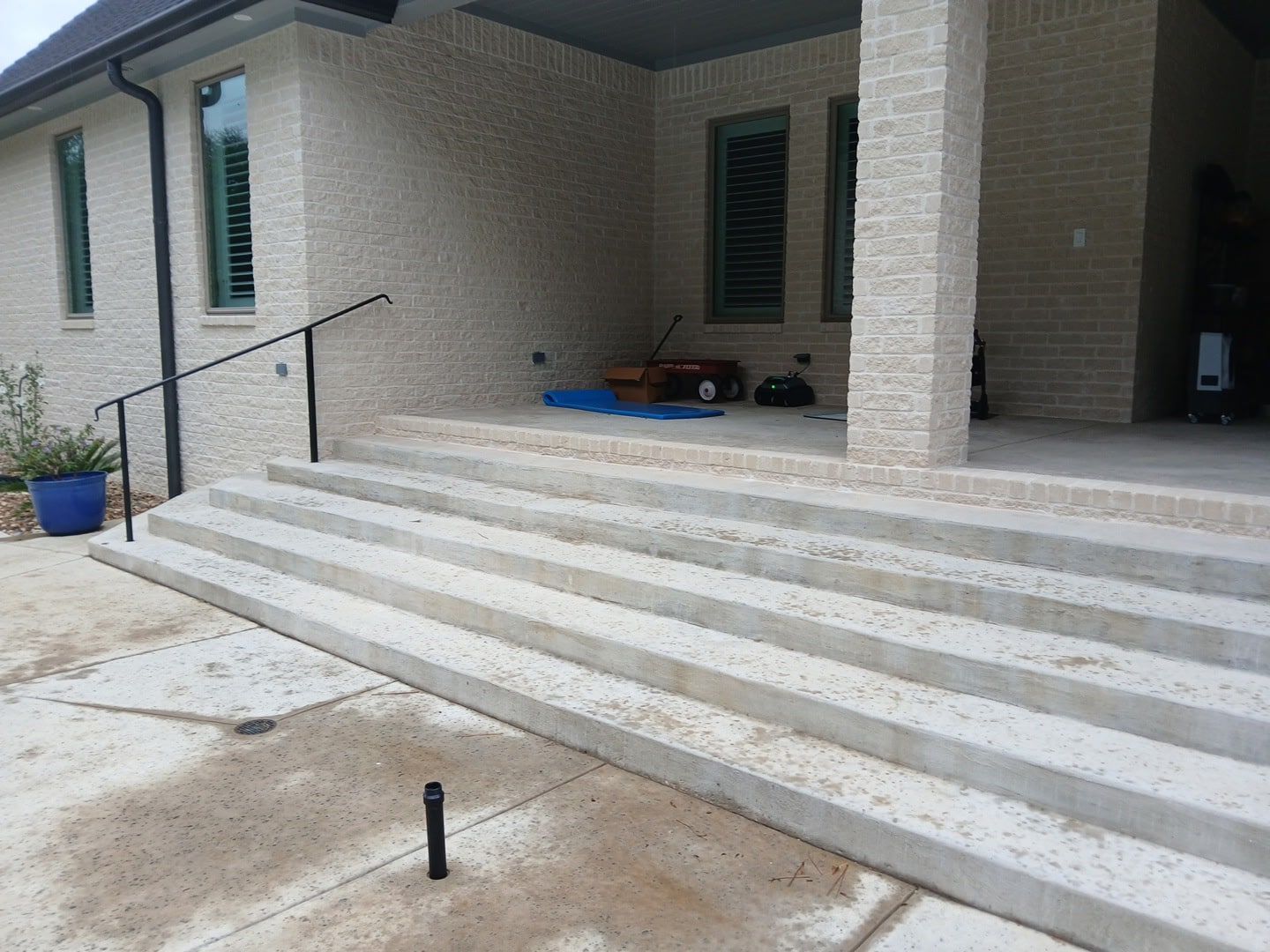 Concrete steps leading up to a house with a porch. A black handrail is present.