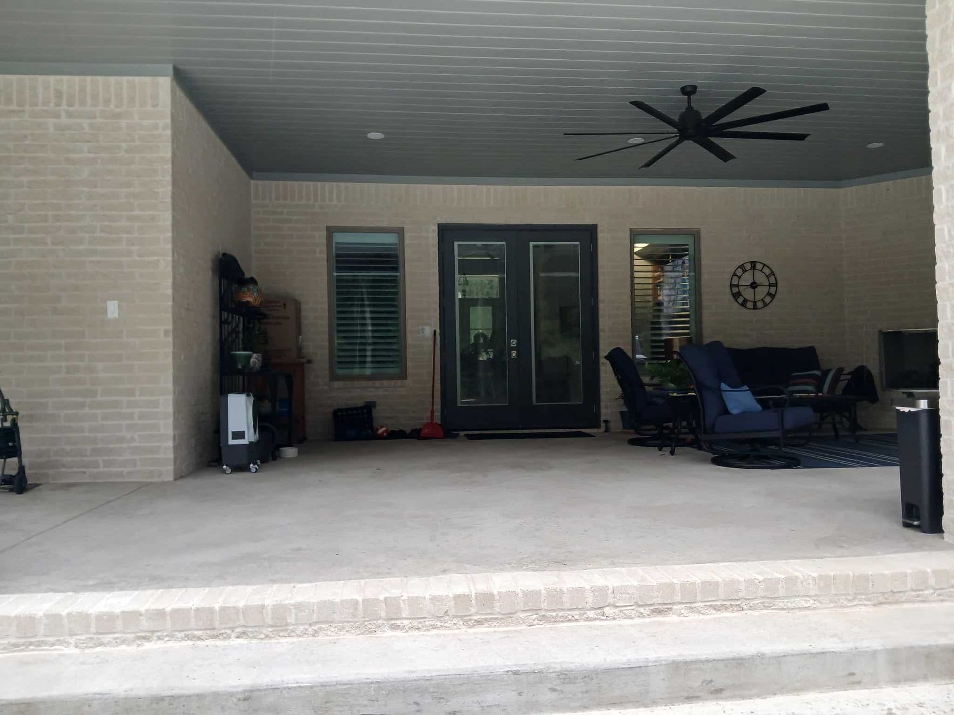 Covered patio with seating, door, fan, and brick walls.