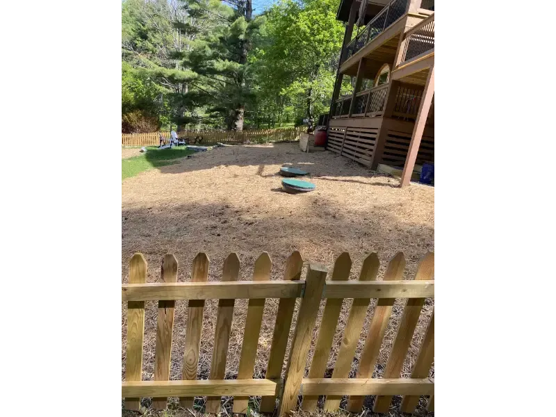 Backyard with wooden fence, gravel ground, trees, and a house deck on the right