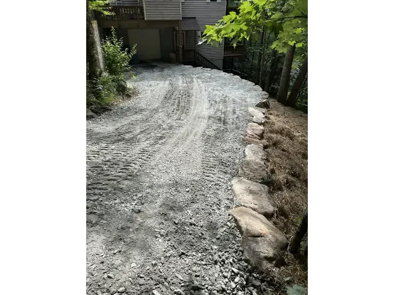 Gravel driveway curving past a house, bordered by rocks and trees