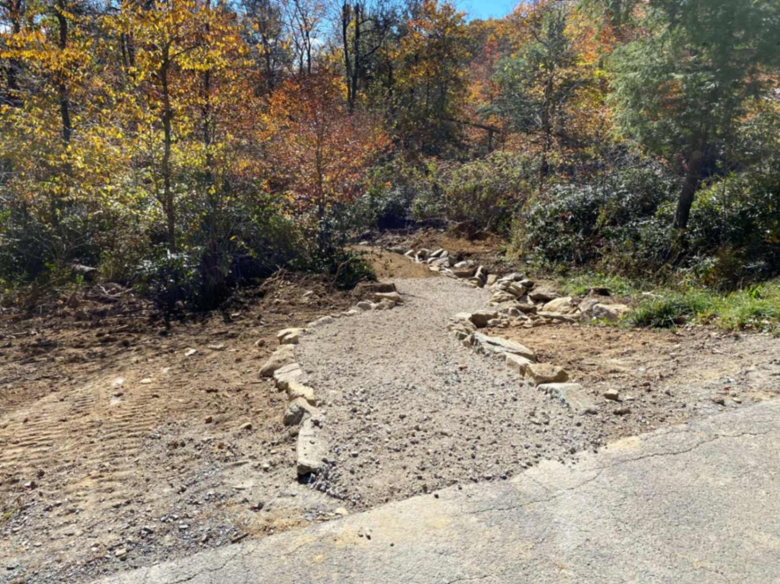 A gravel path with stone edging leads into a wooded area with fall foliage.