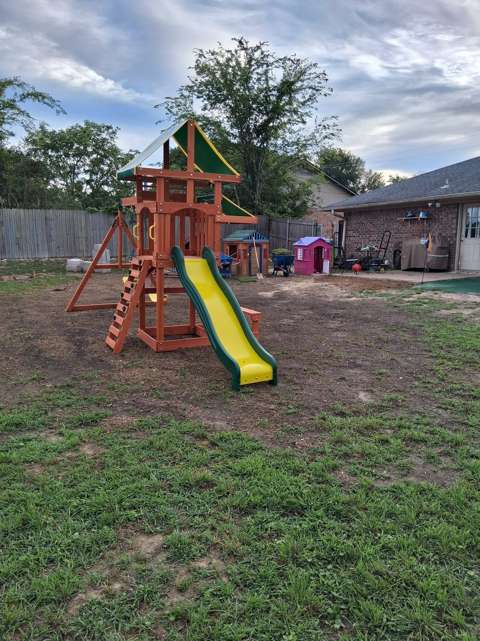 Children’s playset with a yellow slide and wooden climbing frame in a grassy backyard