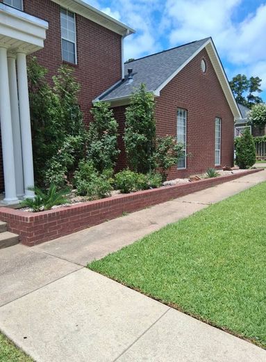 Brick house exterior with landscaped flower bed, sidewalk, and green lawn under a blue sky