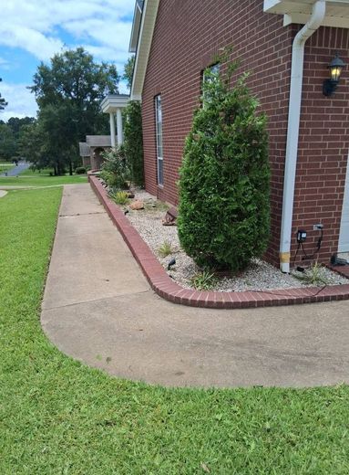 Brick house corner with curved sidewalk, green lawn, and trimmed shrubs along the foundation