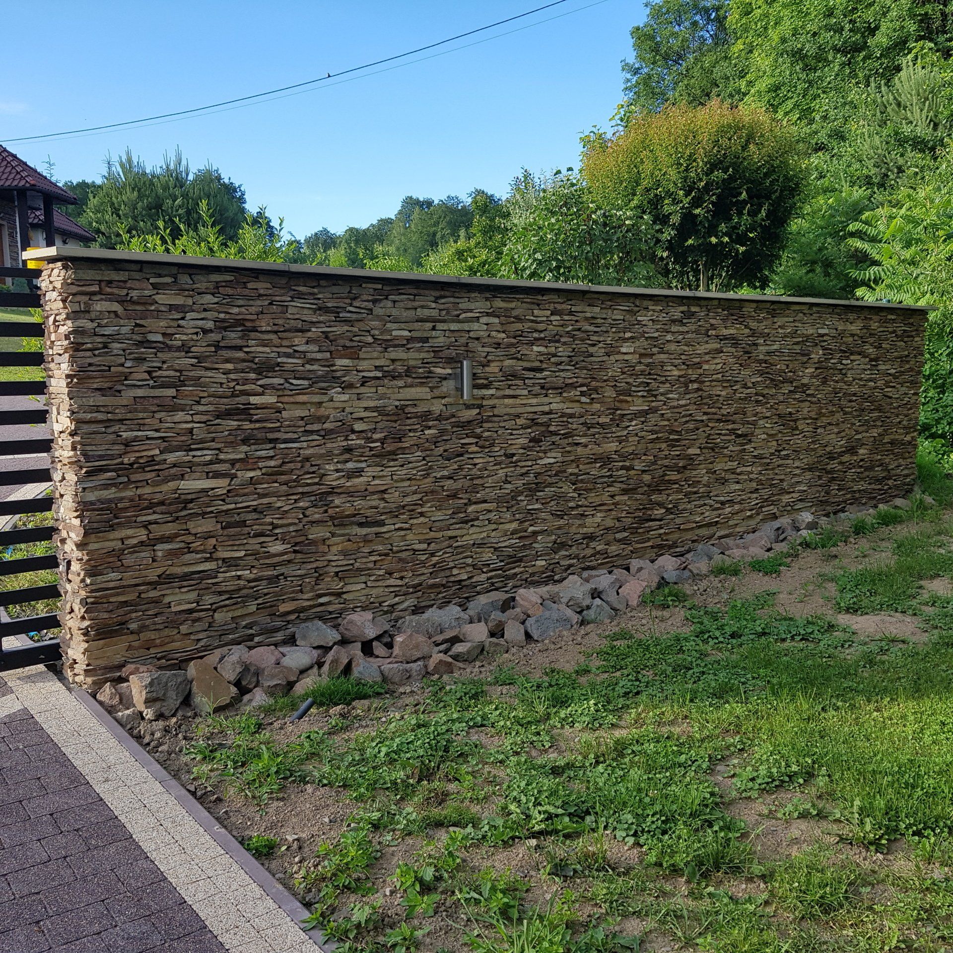 Stone wall in a grassy area, with trees in the background under a blue sky.