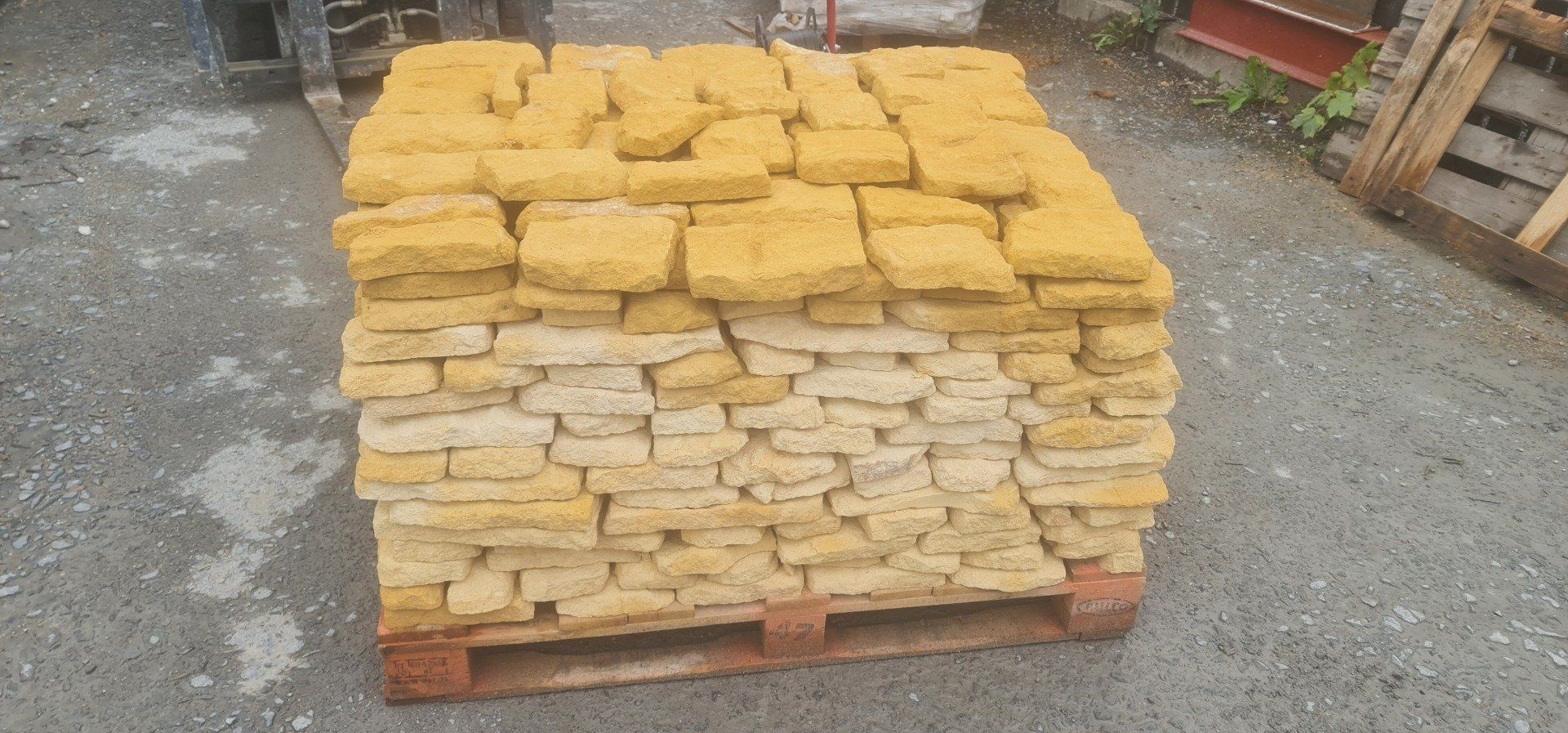 Stack of yellow sandstone blocks on a wooden pallet, outdoors on gray pavement.