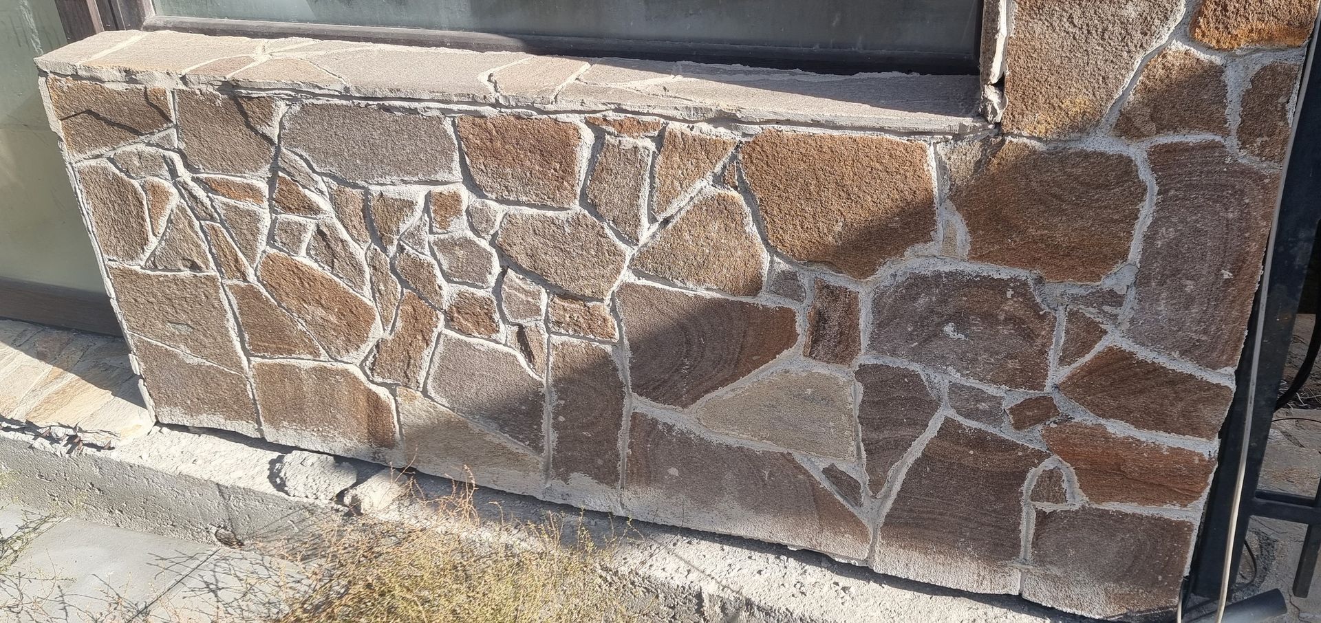 A stone wall composed of various brown and gray stones, mortared together.