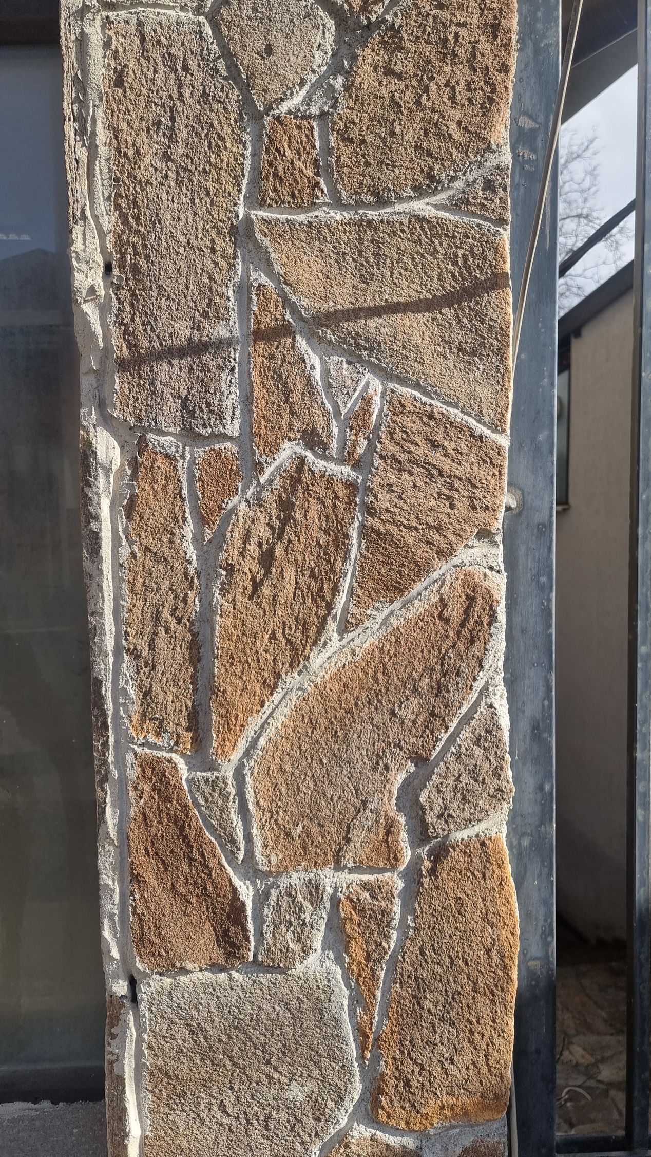 Stone pillar with irregular tan and brown stones, grey grout.