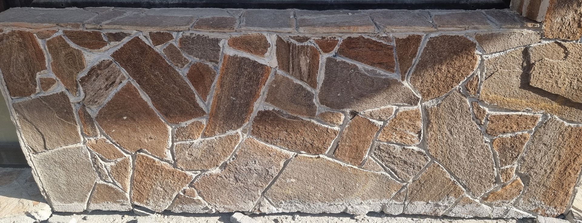 Close-up of a stone wall composed of irregularly shaped, brown and gray pieces. White grout fills the spaces.