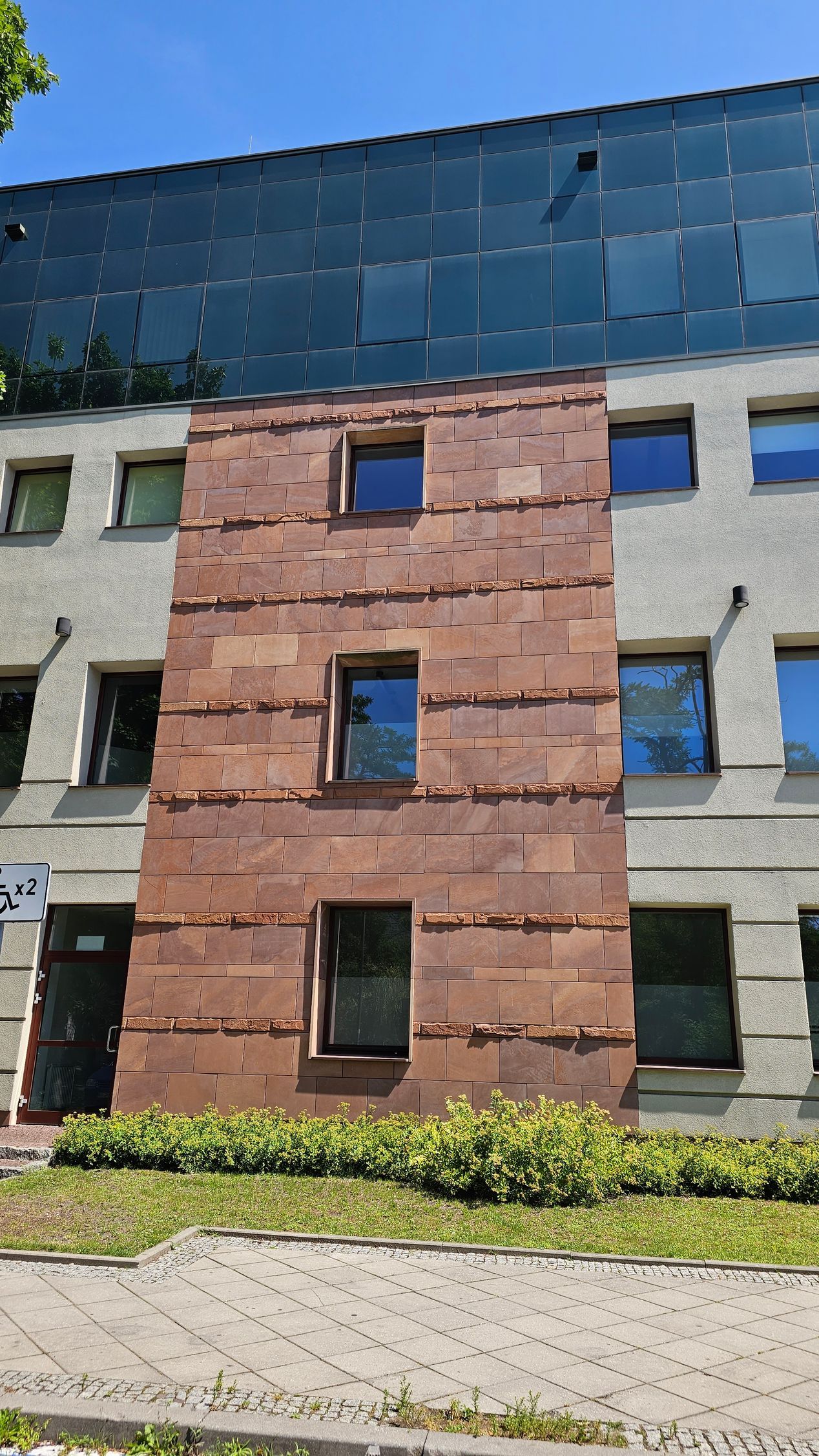 A multi-story building with a reddish-brown brick facade containing three windows. The background is a blue-tinted glass wall.