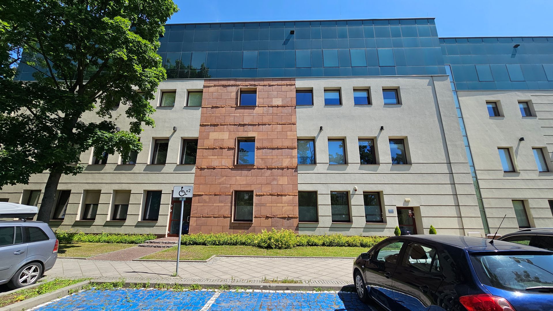 Building exterior with brick accent, several windows, blue sky, and parked cars.