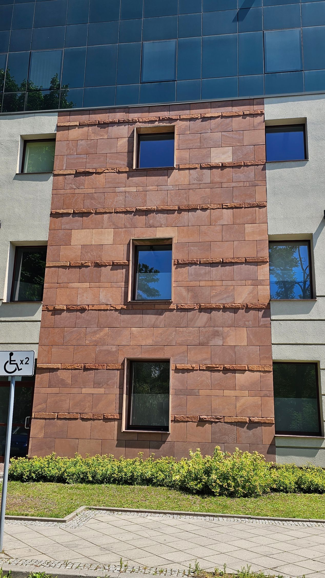 Building facade with red-brown brick-like paneling, three aligned windows, and glass windows above.