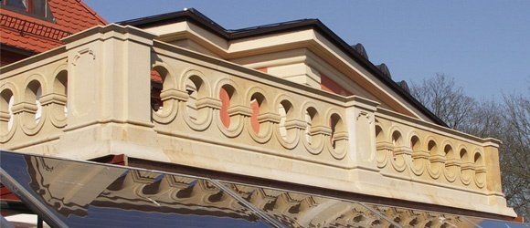 Ornate, light-colored stone balcony with repeating circular and curvilinear cutouts on building exterior.