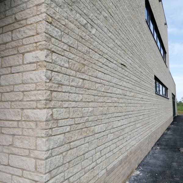 Corner of a building with light gray brick facade and dark-framed windows.